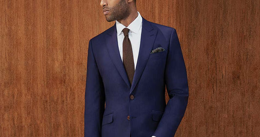 man wearing a navy suit with brown knitted tie against a wooden wall