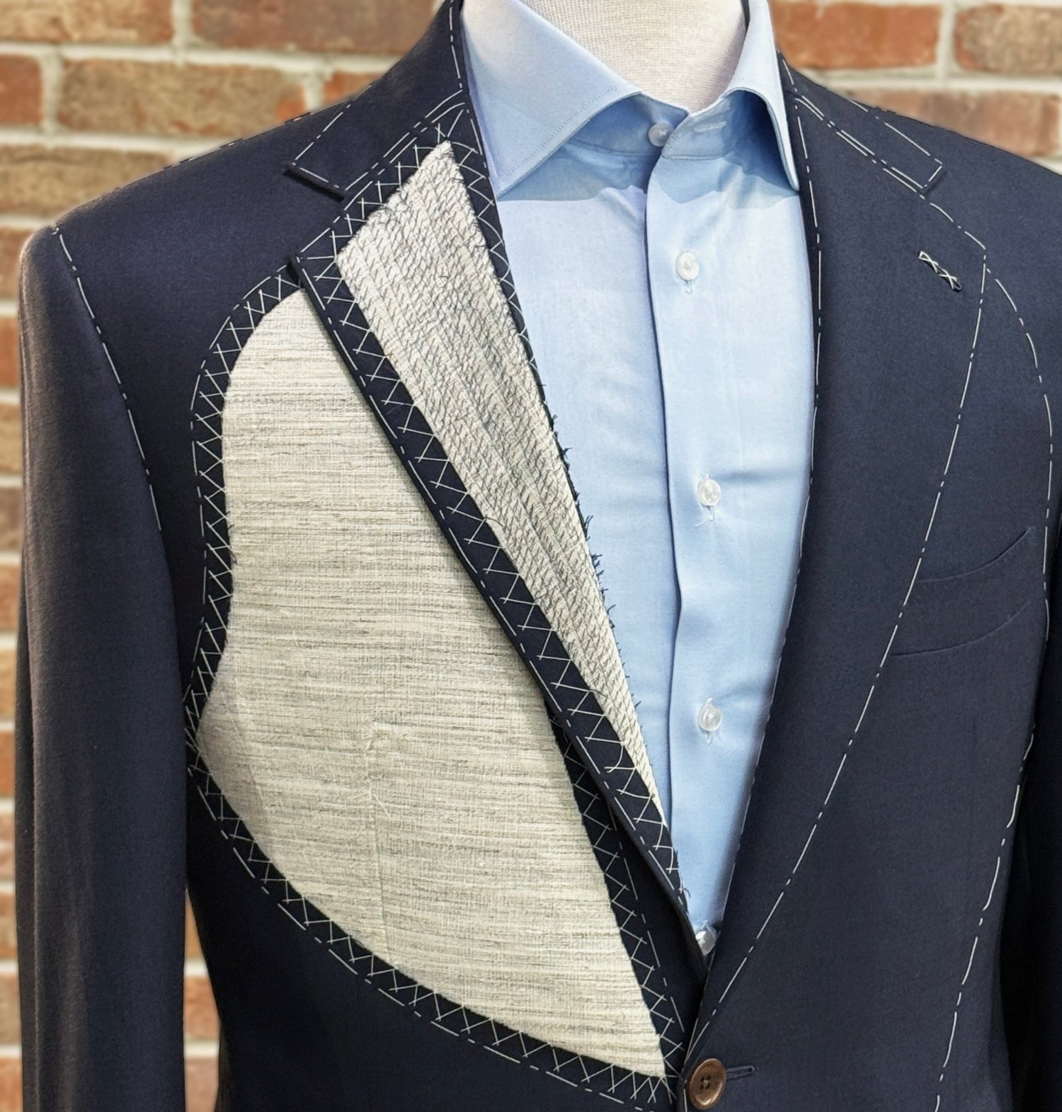 Navy blazer with textured lining on a mannequin against a brick wall.
