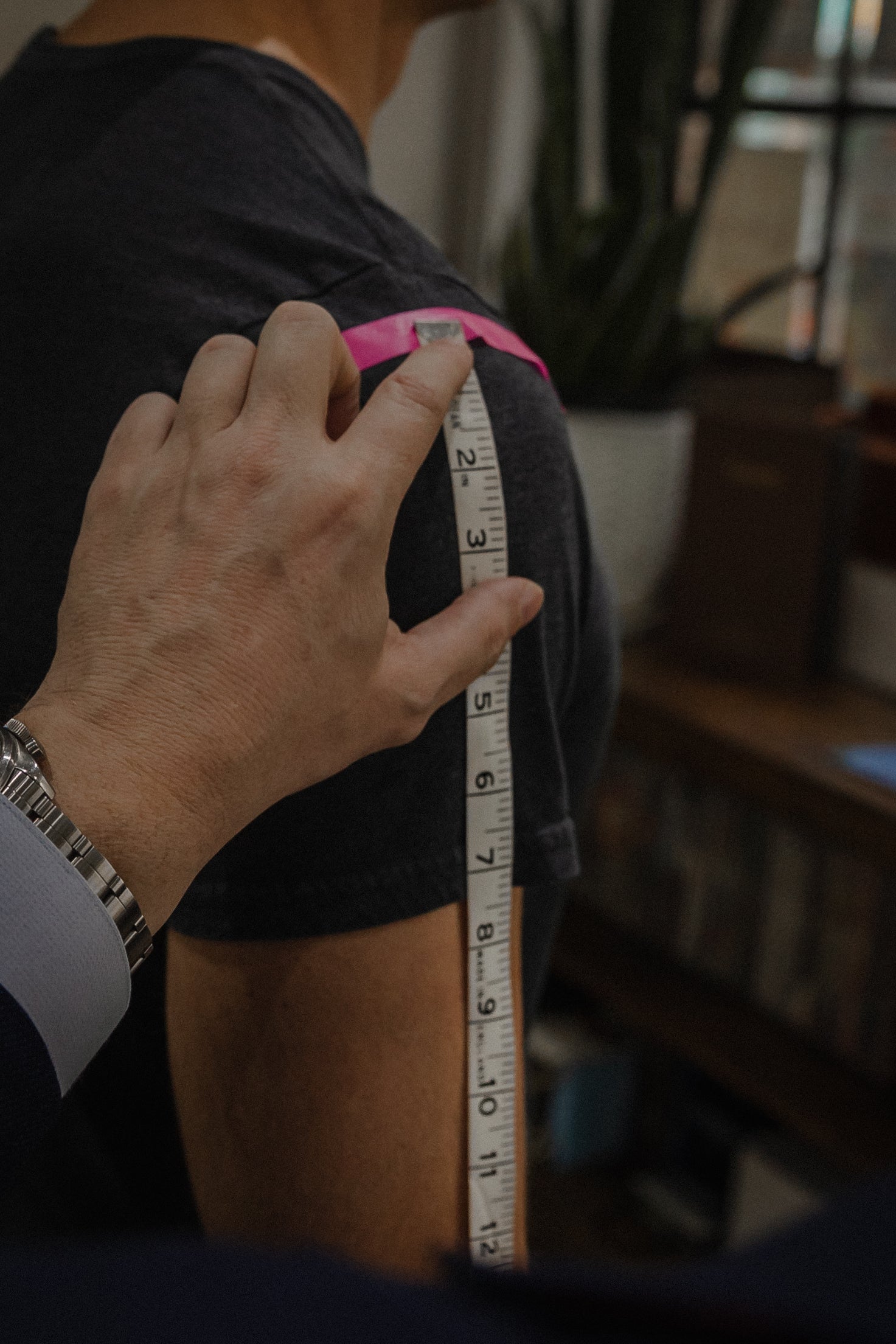 Person measuring another person's arm with a tape measure indoors.