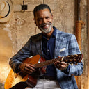 man wearing blue checked blazer and holding a guitar