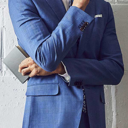 man wearing blue suit with arms crossed with suit pockets showing