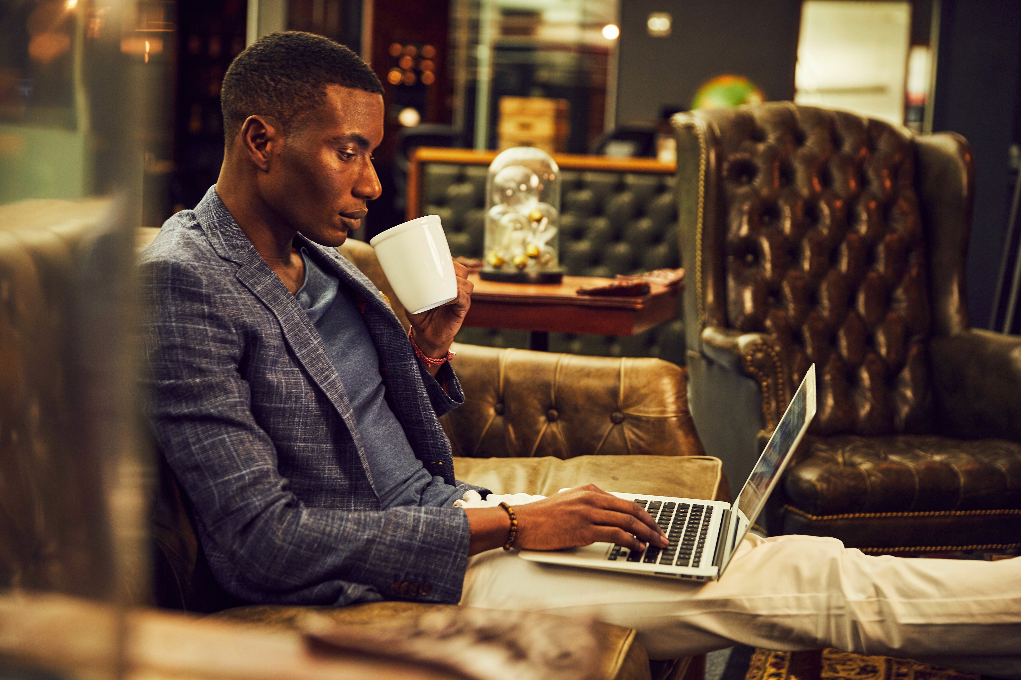 Man using a laptop in a cozy, dimly lit room with leather furniture.