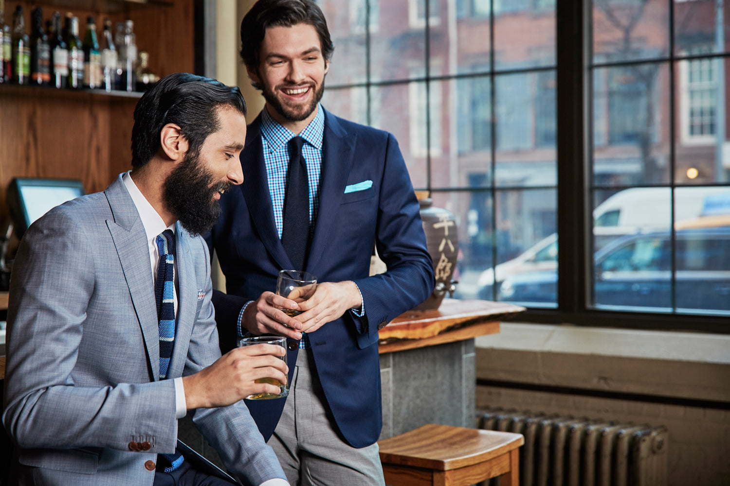 Two men in suits standing in a bar, holding drinks.